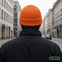 Person wearing an orange beanie on a city street, face partly shown from behind