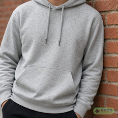 Person in a grey hoodie leaning on a brick wall, face not shown
